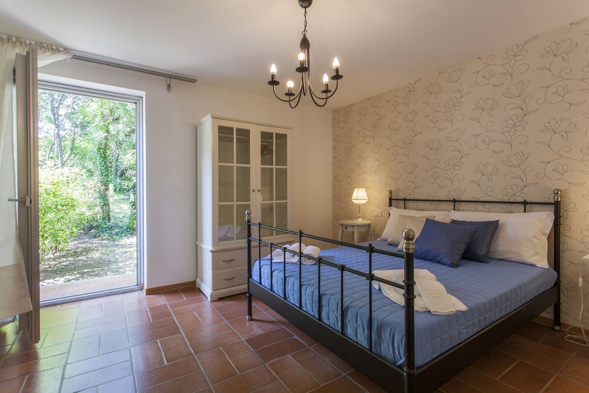 Un dormitorio con cama, mesita de noche, cómoda, candelabro y vistas al exterior.