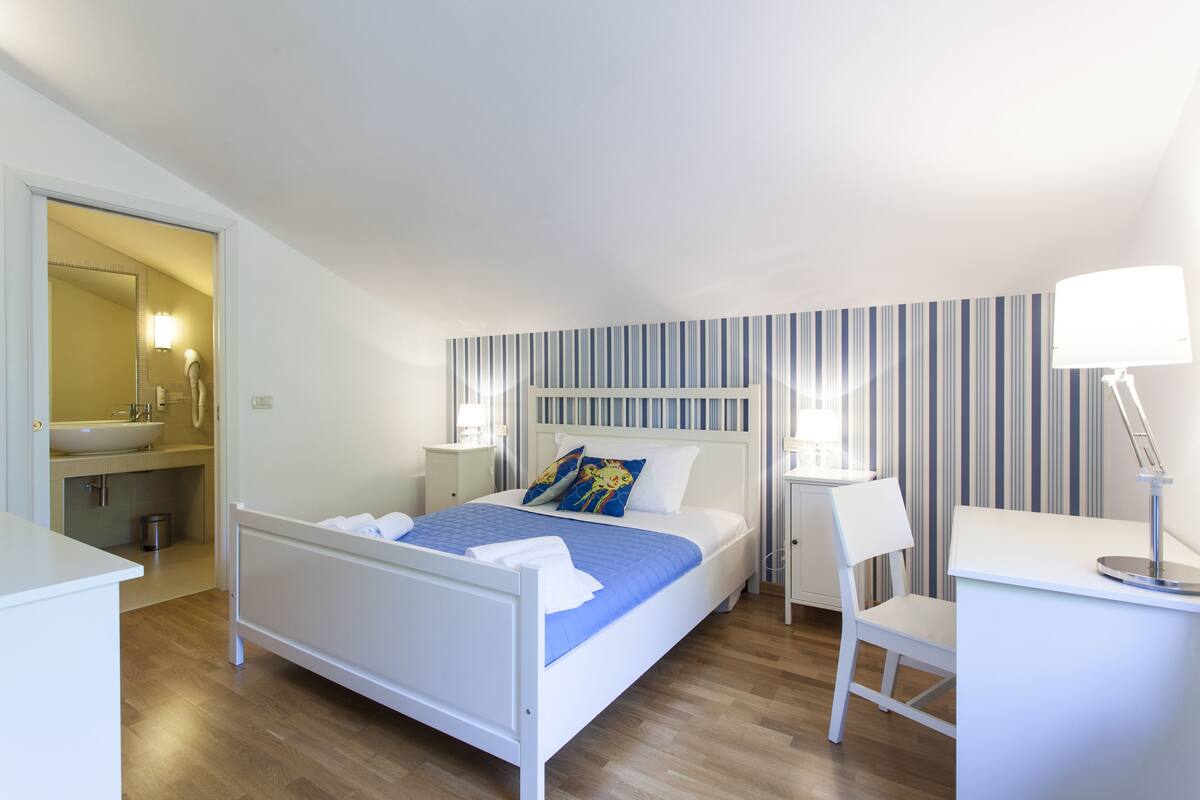 Un dormitorio con cama, mesitas de noche, escritorio y una silla.
