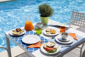 A dining table by a pool with breakfast items, a pitcher of orange juice, and a potted plant. - Villa Borgo Duino (Duino-Aurisina)