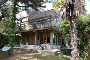 Een modern huis met twee verdiepingen, een balkon, grote ramen en een tuin met een hangmat.