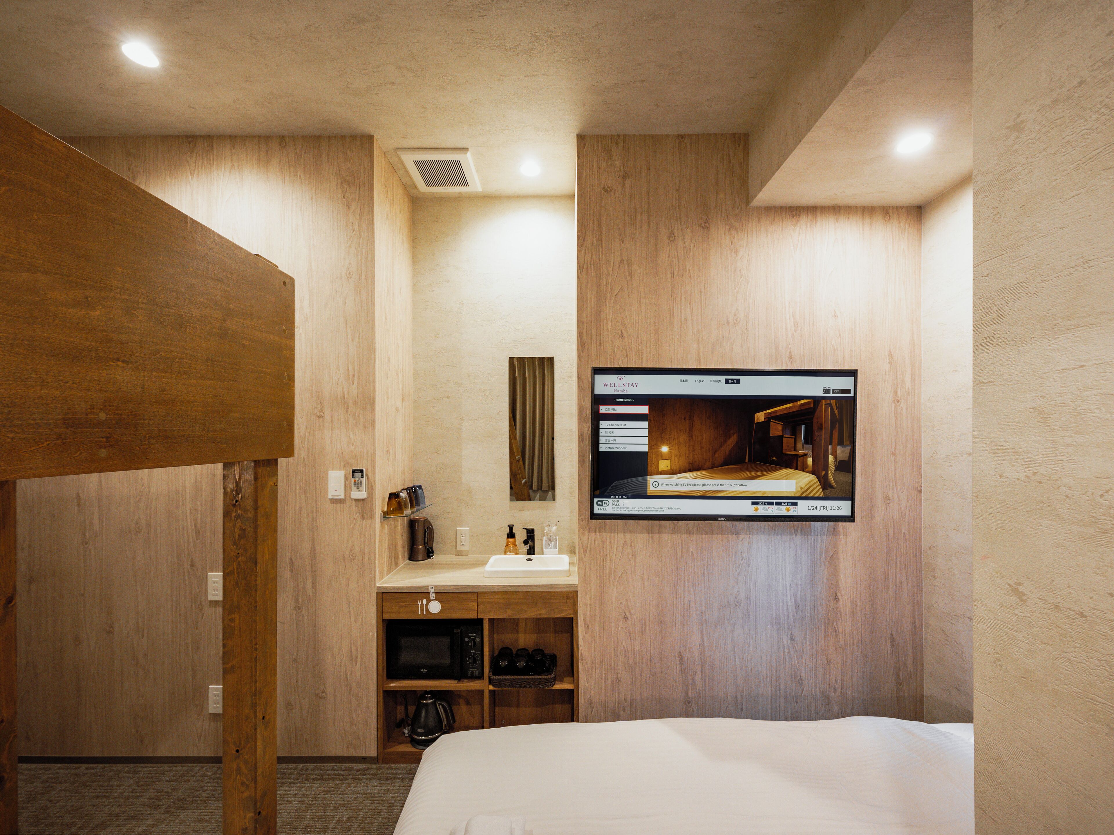 Une chambre d’hôtel avec un intérieur en bois, un lit, un téléviseur fixé au mur, une petite kitchenette et une armoire en bois.