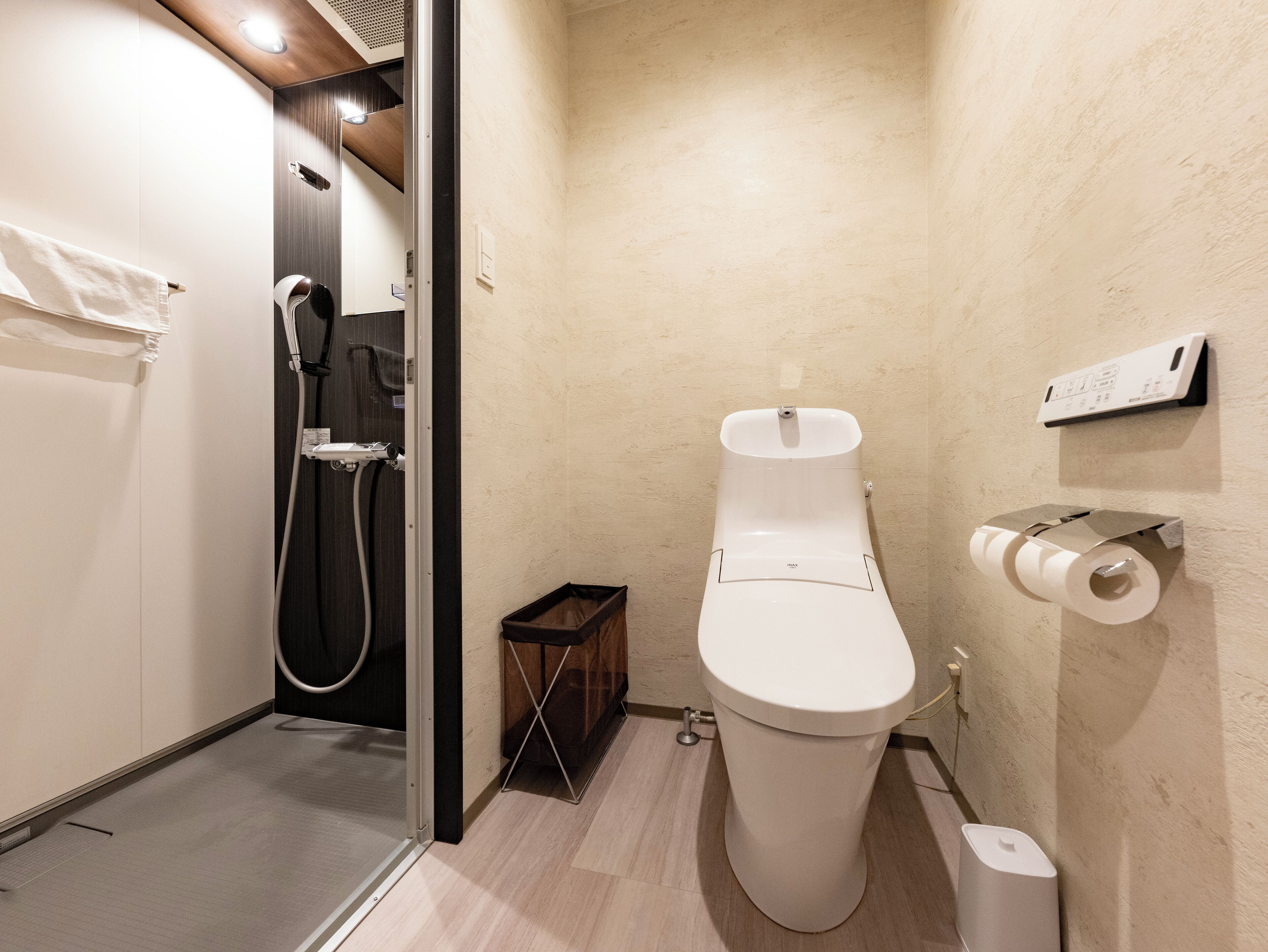A compact bathroom with a toilet, a shower, and a toilet paper holder.
