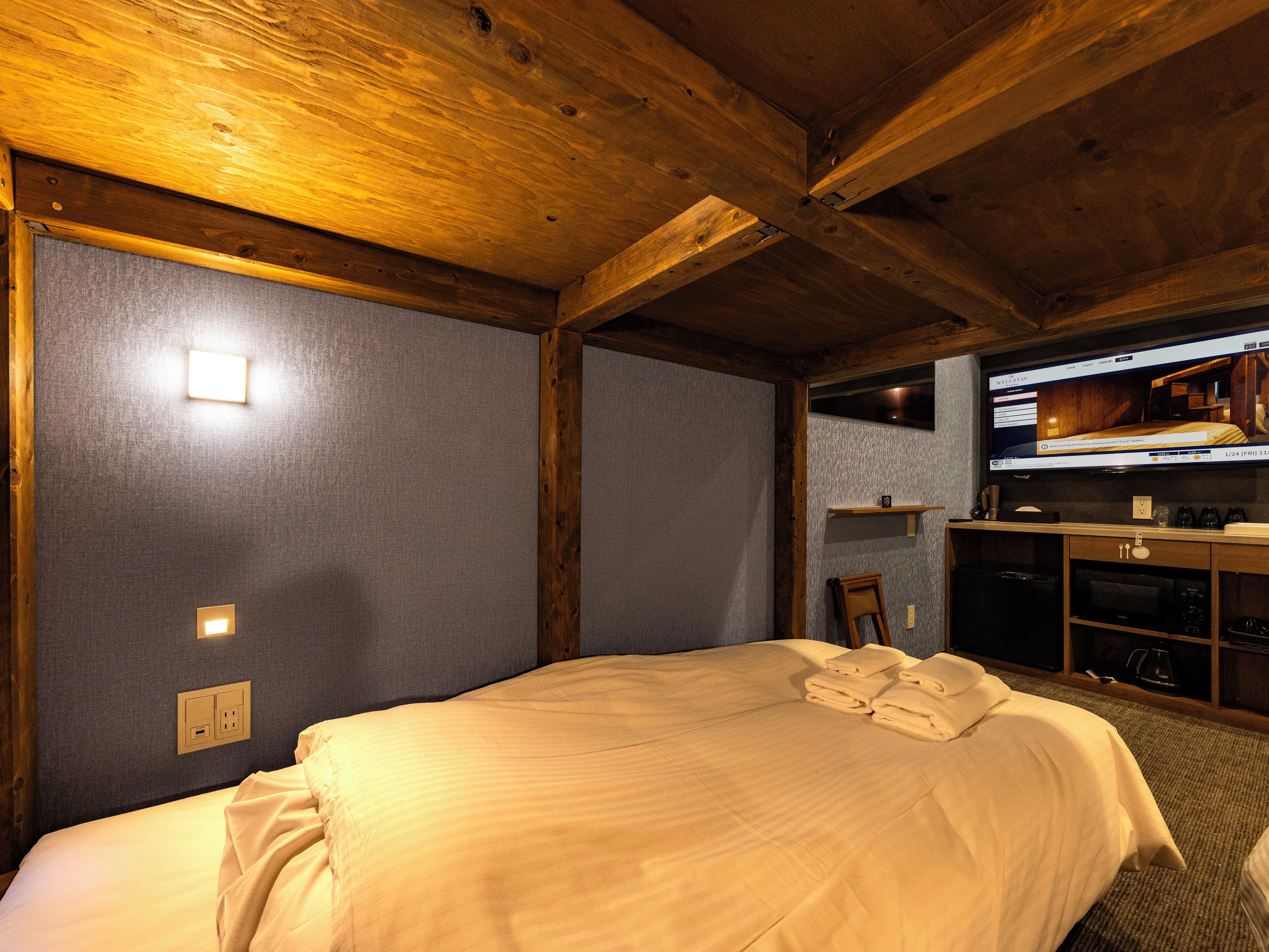 A hotel room with a bed, a television, and a small kitchenette.