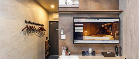 A modern bathroom with a large mirror, a sink, and a television displaying a room.