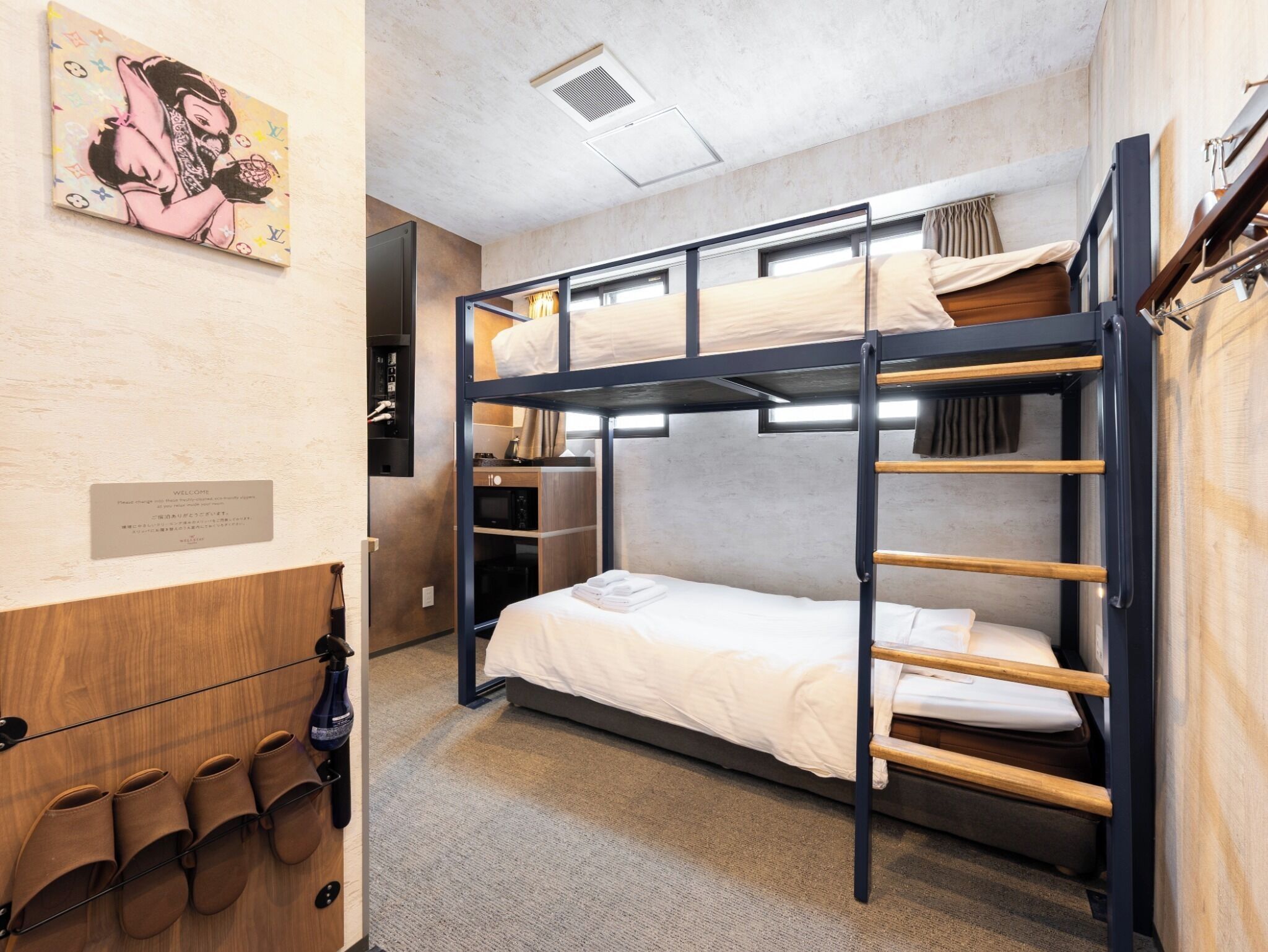 Een slaapkamer met een stapelbed, een houten garderobe, een welkomstbord en een kunstwerk aan de muur.