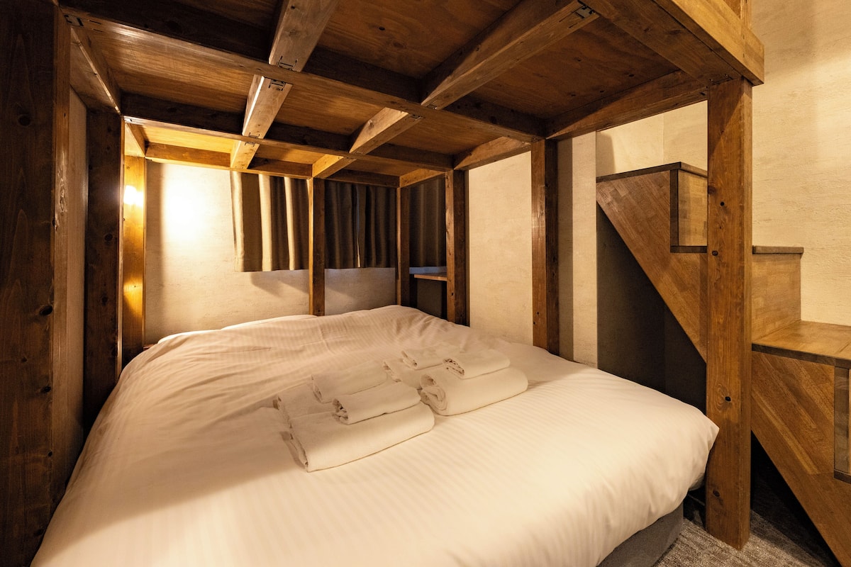 Ein Zimmer mit Holzboden, einem Bett, einer Treppe und einem Fenster mit Vorhängen.