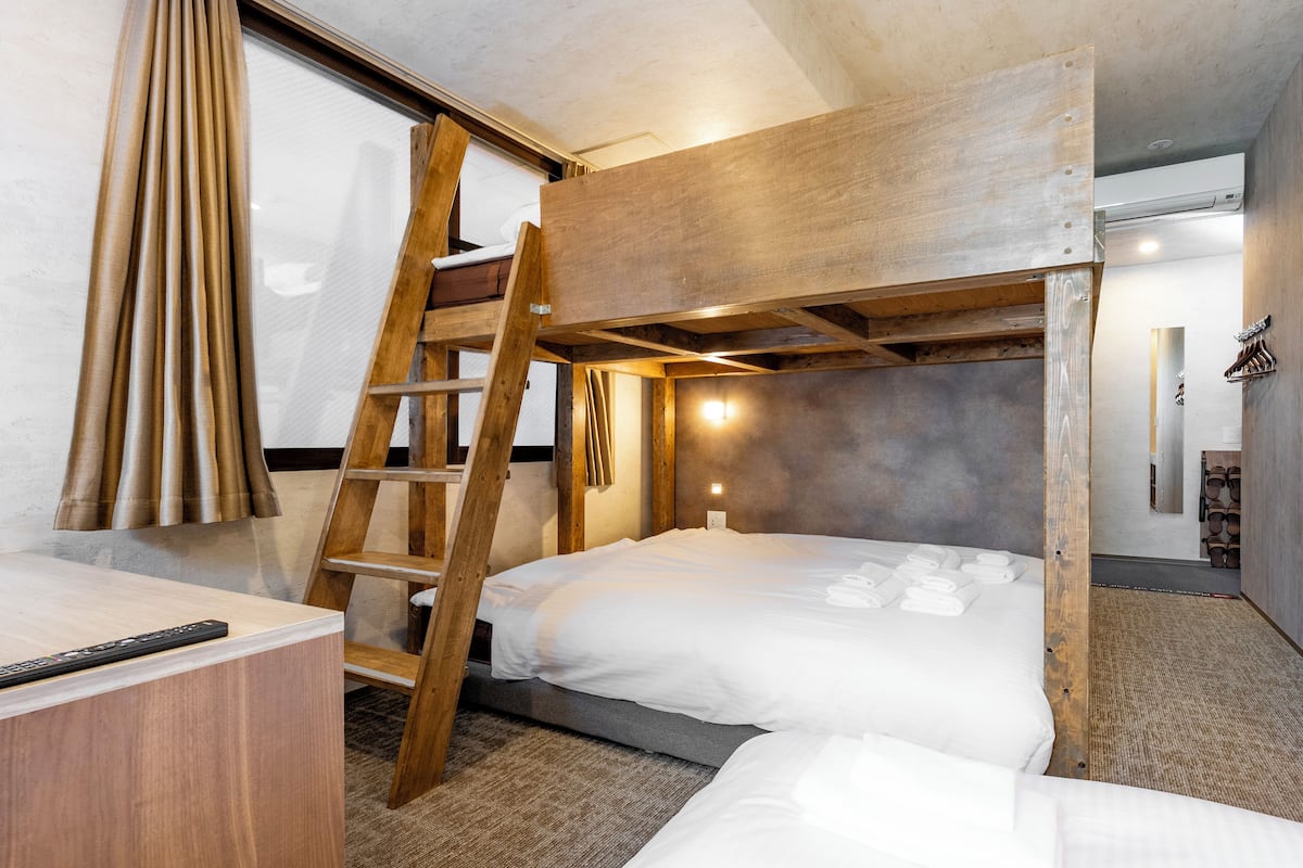 Ein Schlafraum mit Etagenbett, Holzleiter, Schreibtisch und Fernbedienung.