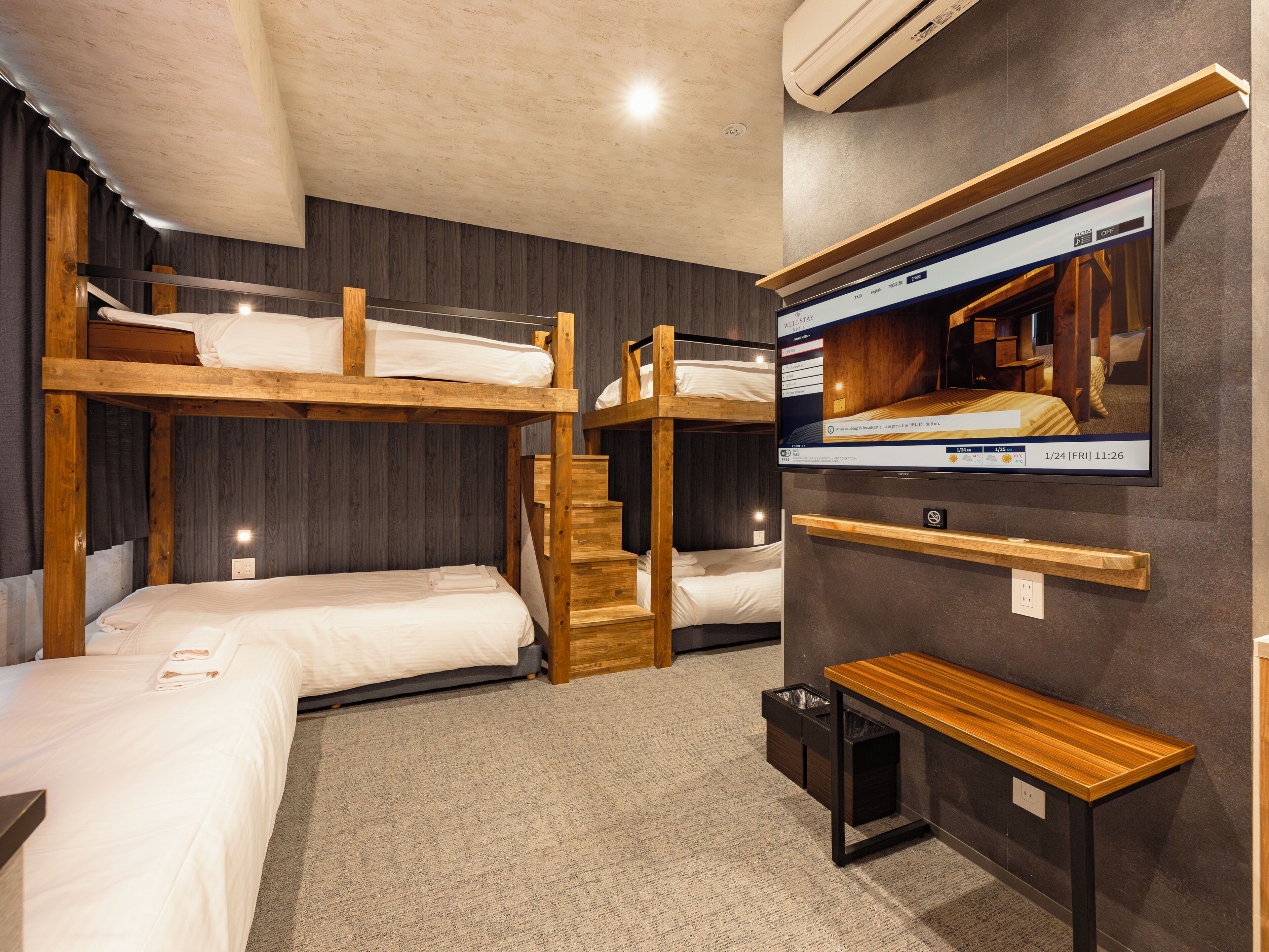 A room with bunk beds, a TV mounted on the wall, and a small wooden table.