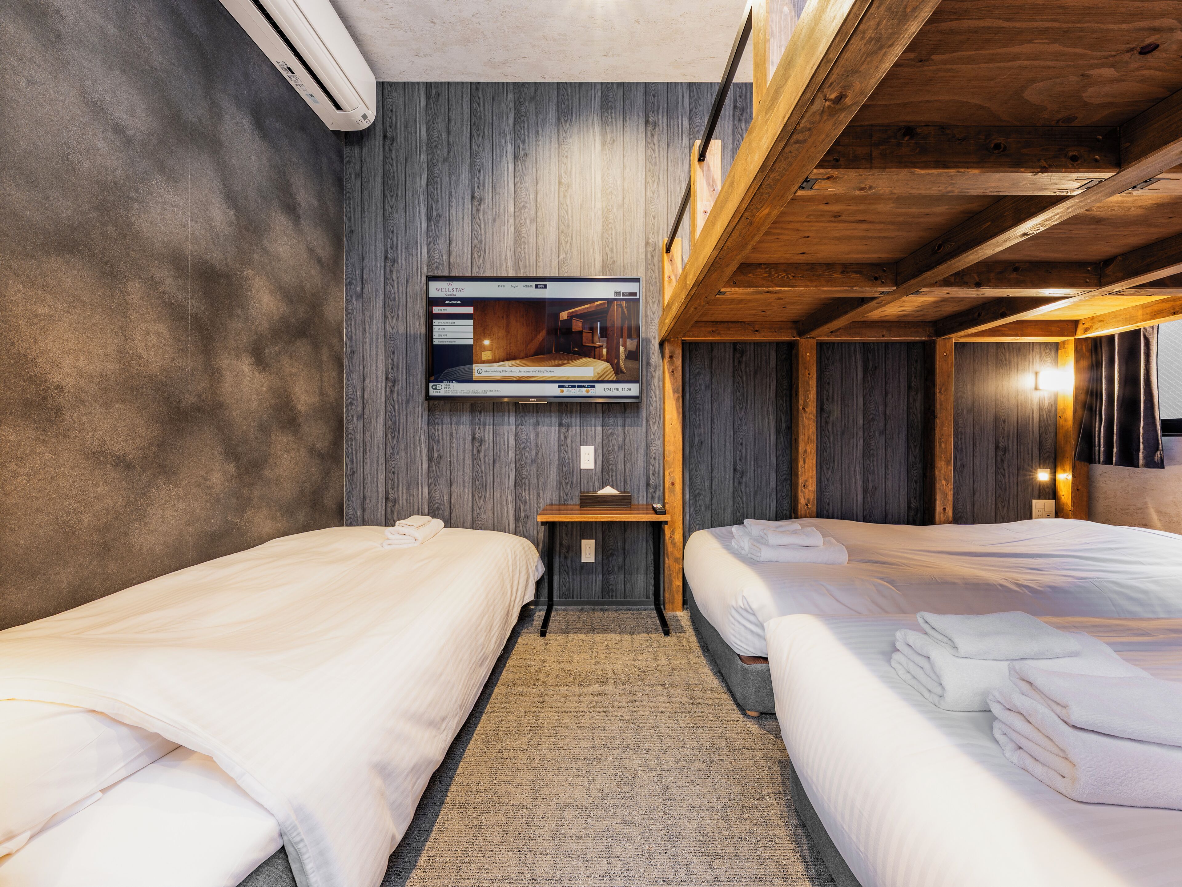 Quarto de hotel com duas camas, televisão fixada na parede e teto de madeira.