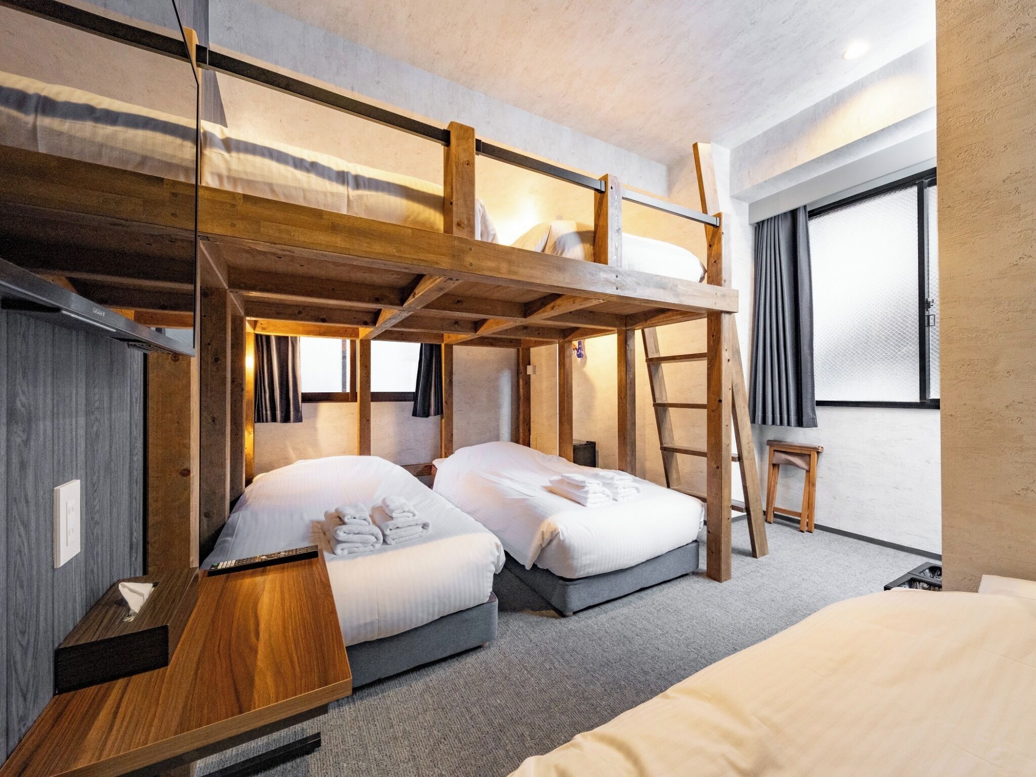 Een slaapkamer met een stapelbed, een houten ladder en een raam met gordijnen.