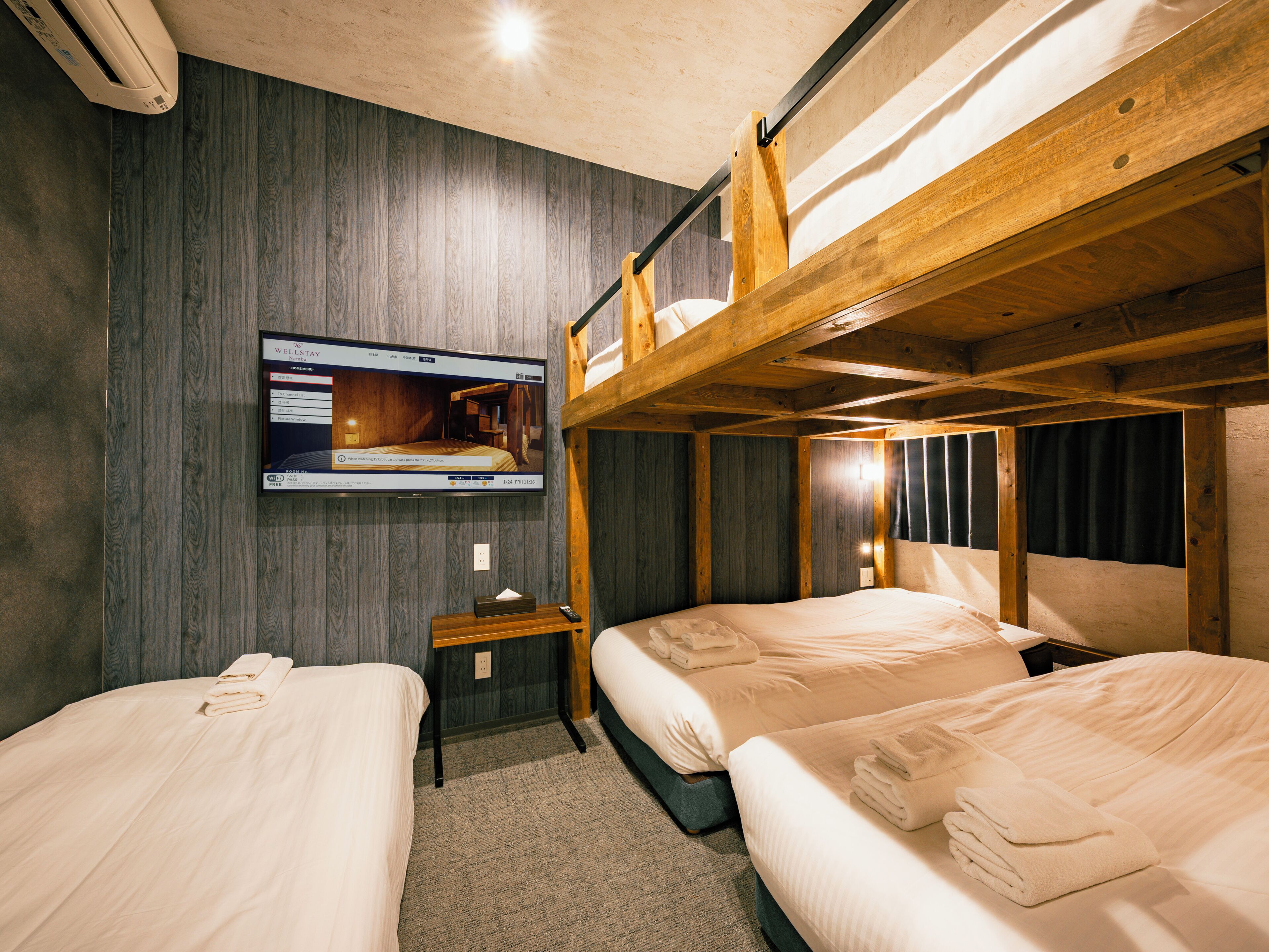 A room with two beds, a television mounted on the wall, and a bunk bed above.