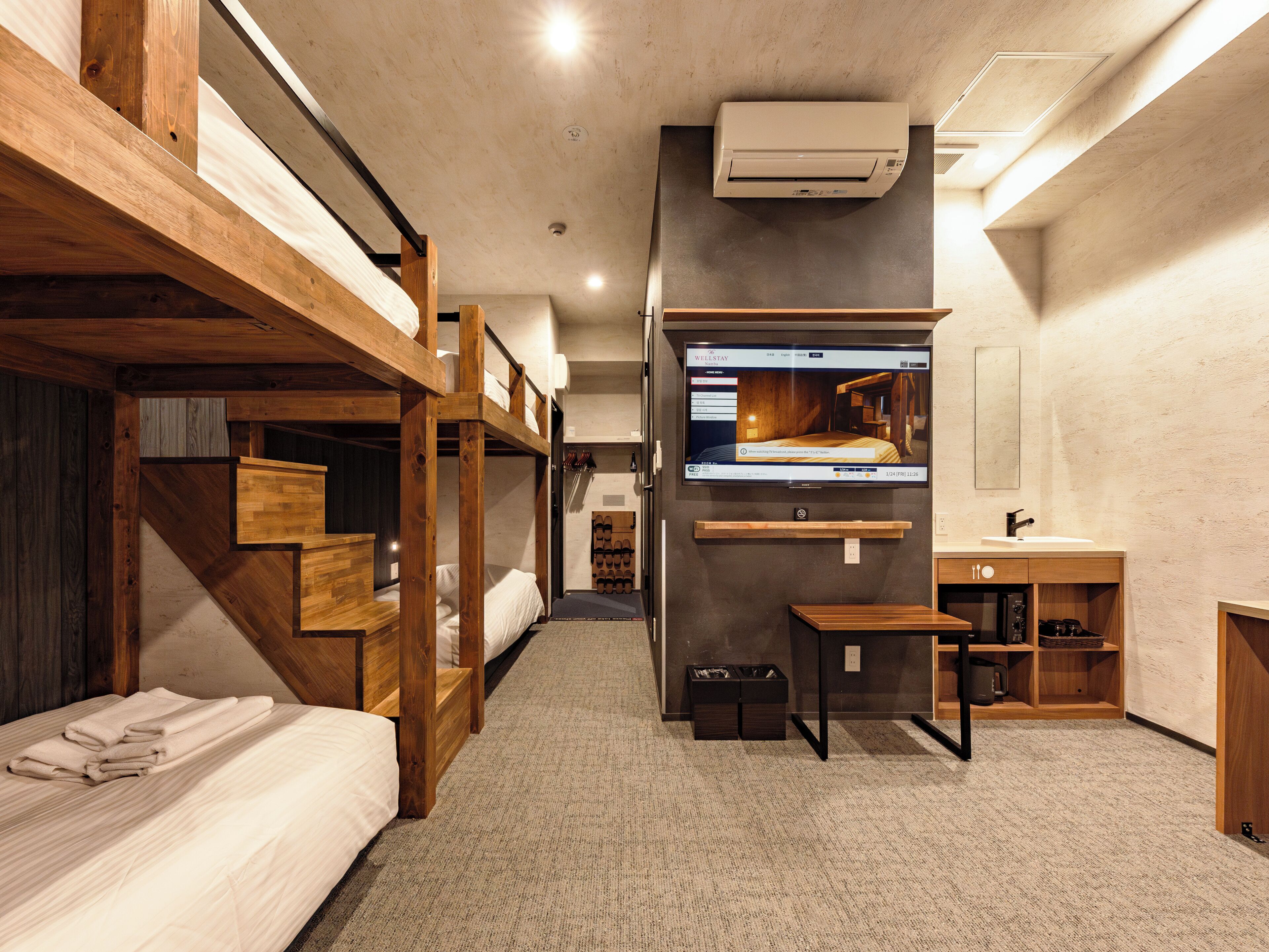 A room with bunk beds, a television mounted on the wall, a sink, and a small table.