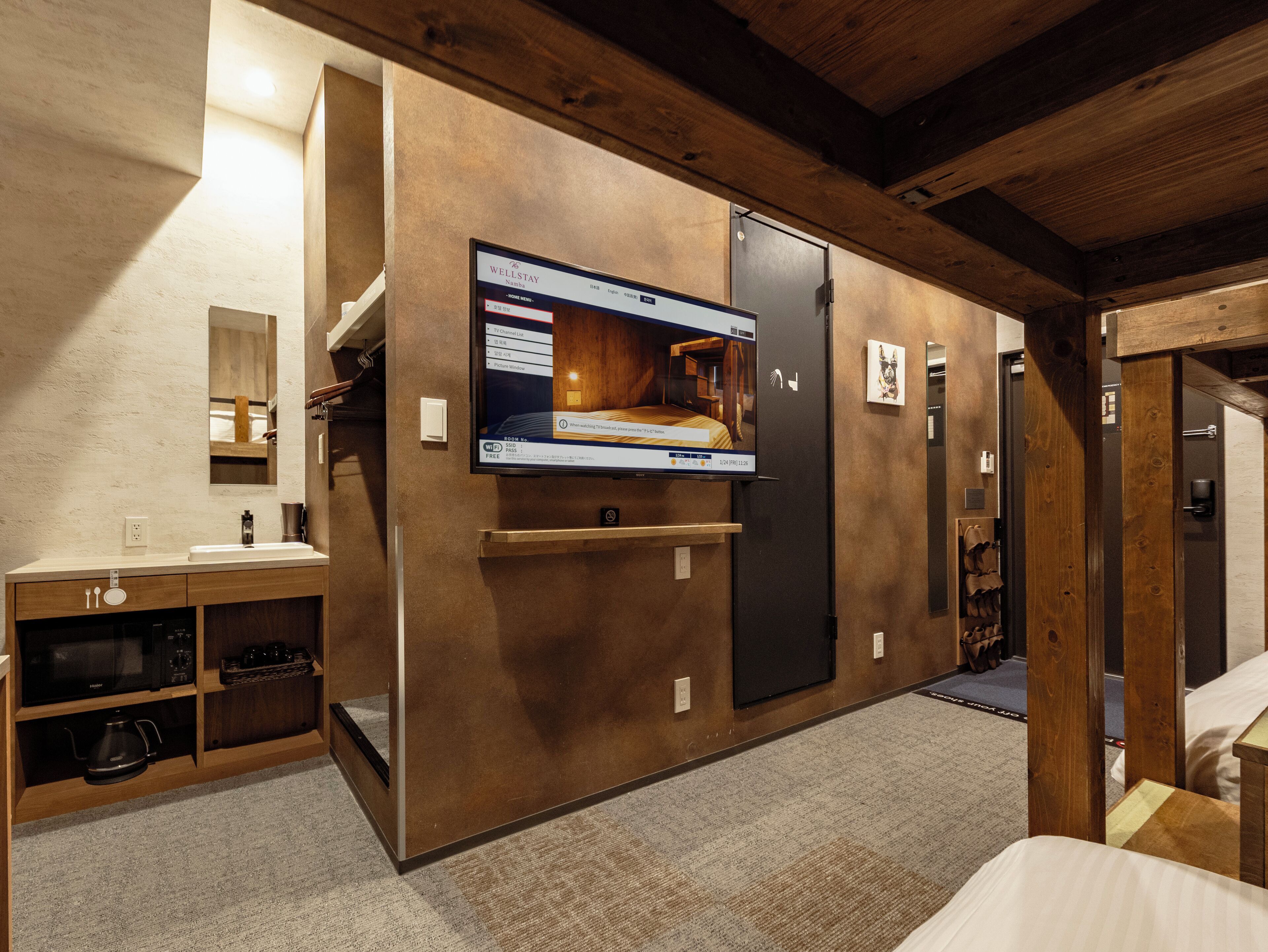 Una habitación de hotel moderna con una amplia televisión de pantalla plana montada en la pared, un mueble de madera con microondas y un refrigerador pequeño.