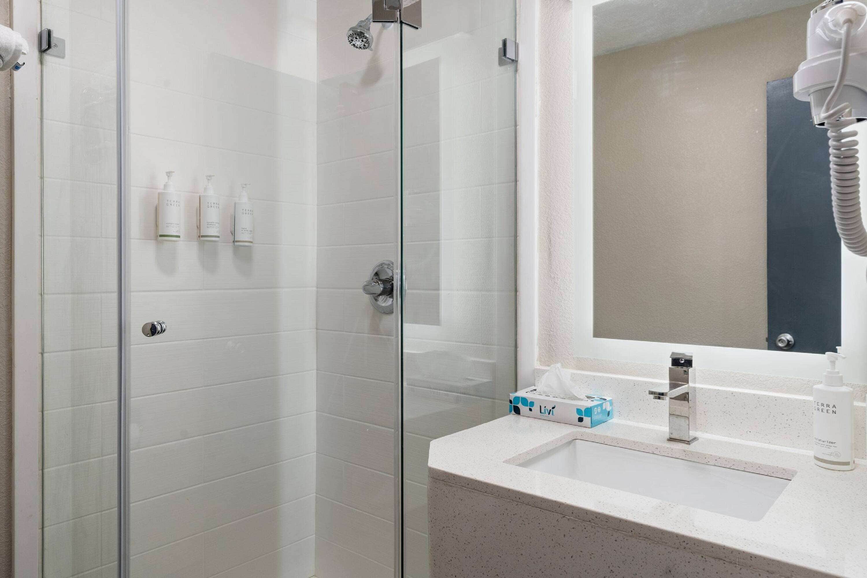 A modern bathroom with a glass shower enclosure, a sink with a mirror, and toiletries on the countertop.