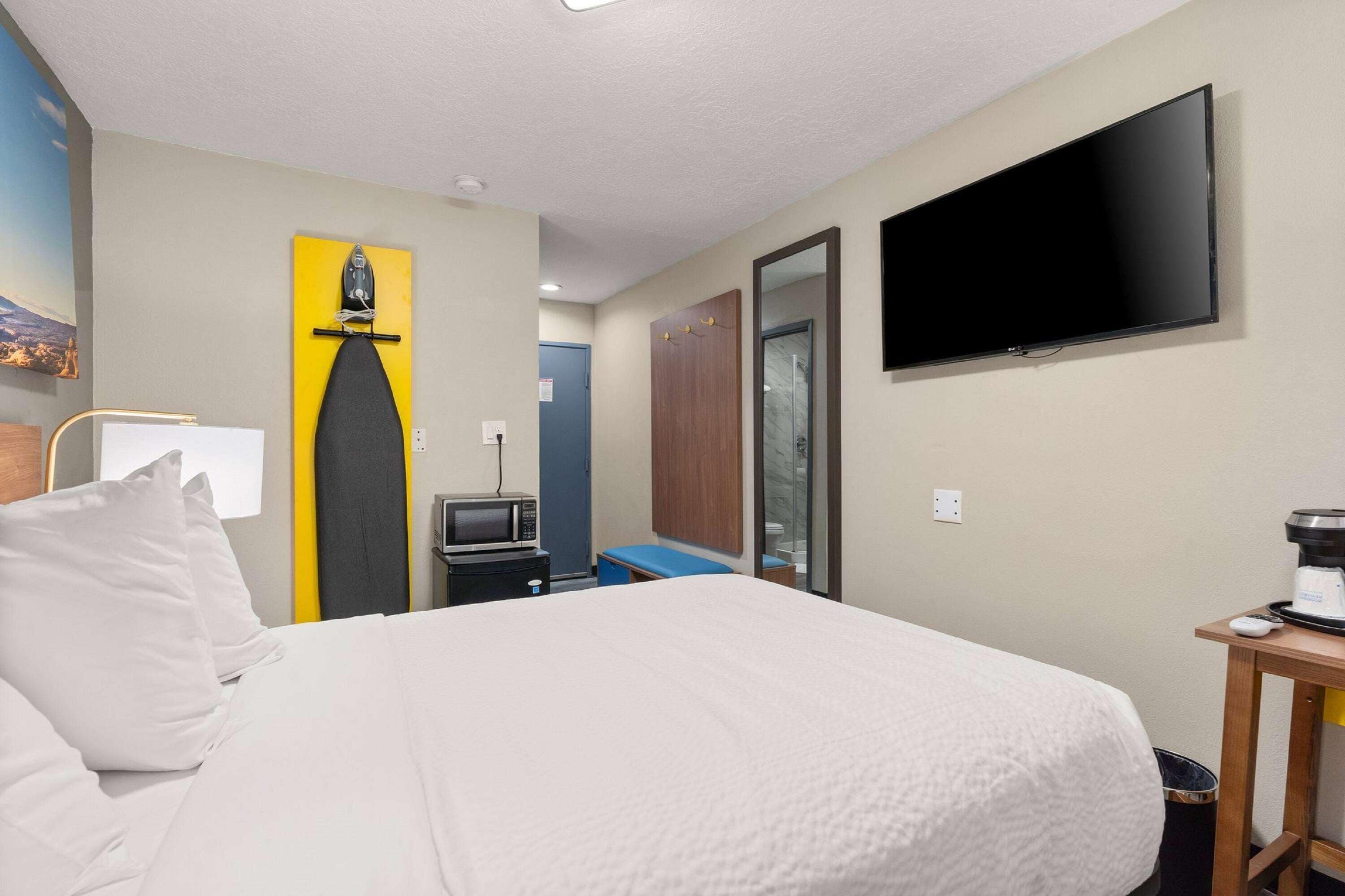 Habitación de hotel con cama, televisor de pantalla plana, microondas, cafetera y puerta con espejo.
