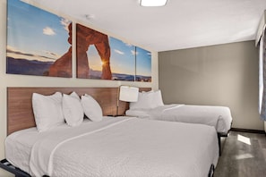 A hotel room with two beds, a wooden headboard, a nightstand, a lamp, and a large wall painting of a rock formation. - Days Inn by Wyndham Albuquerque I-25 (Albuquerque)