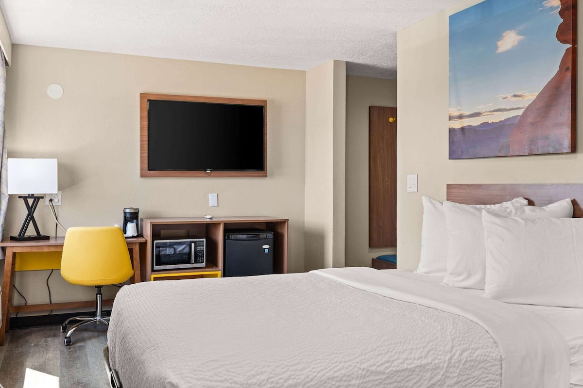 A hotel room with a bed, a desk with a chair, a television, and a painting on the wall.
