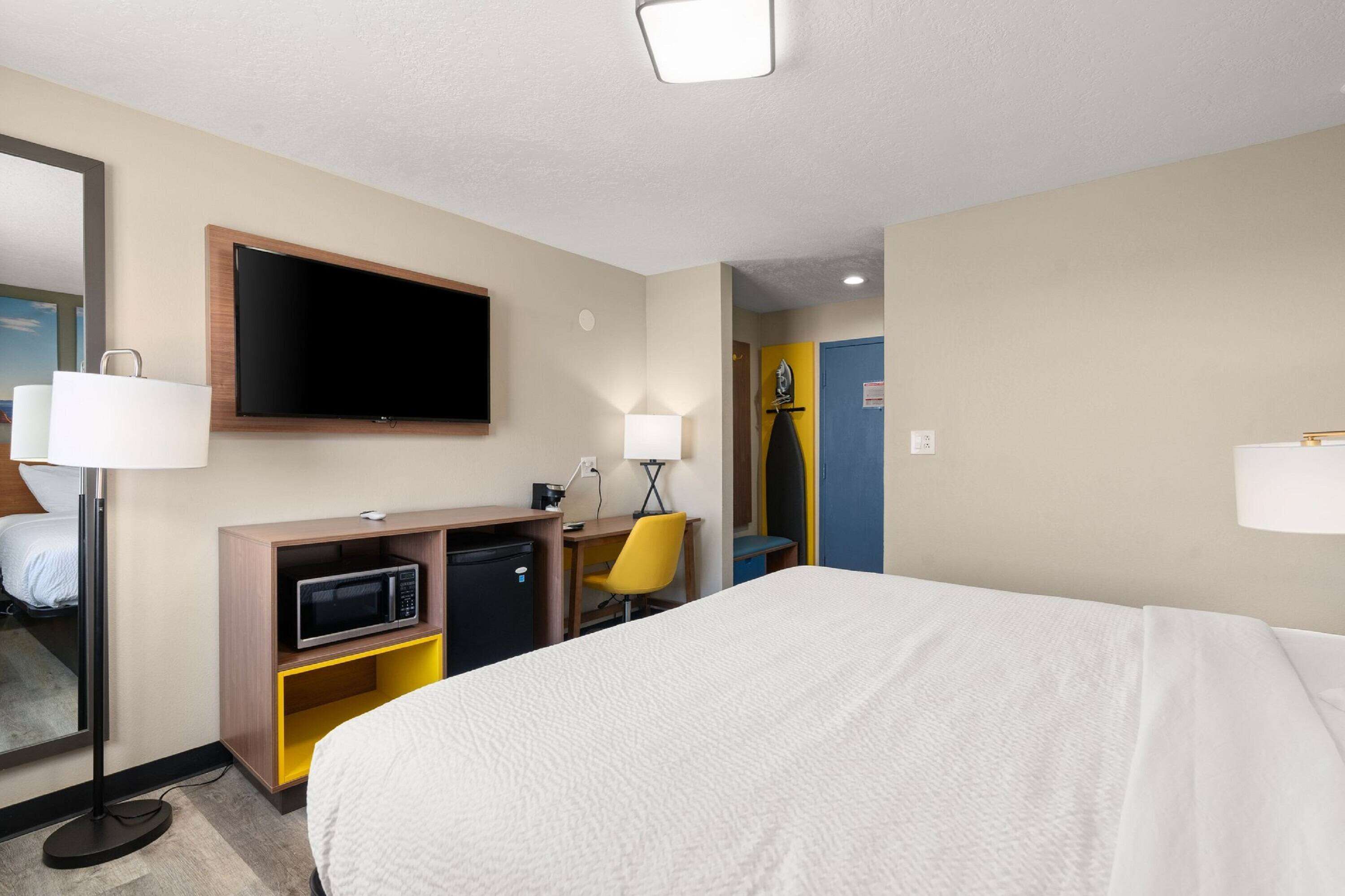 A hotel room with a bed, a desk with a computer, a microwave, and a TV.