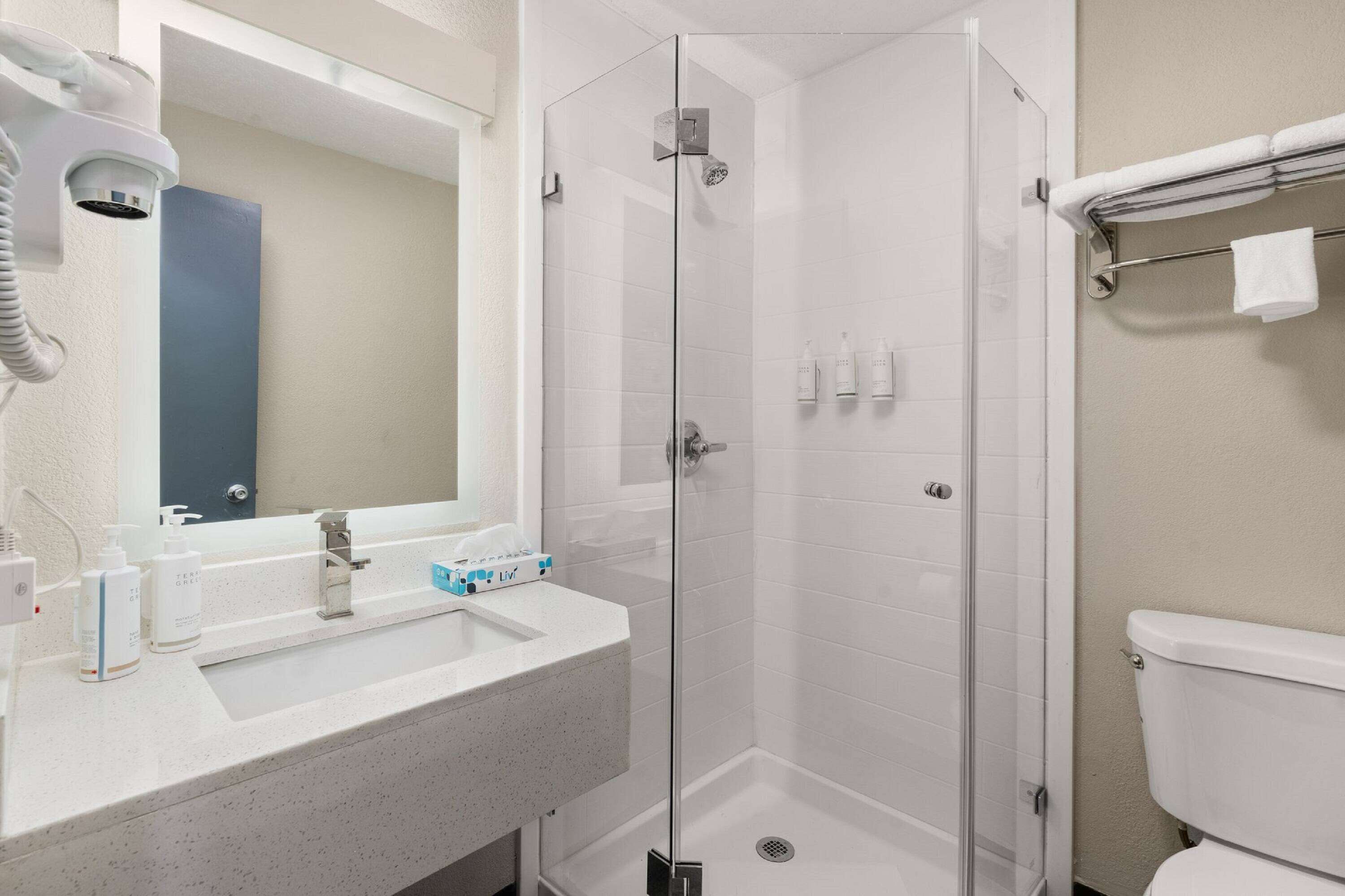 A bathroom with a glass-enclosed shower, a sink with toiletries, and a towel rack.
