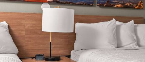 A hotel room with a wooden headboard, white bedding, a bedside table with a lamp, and a landscape painting above the bed.