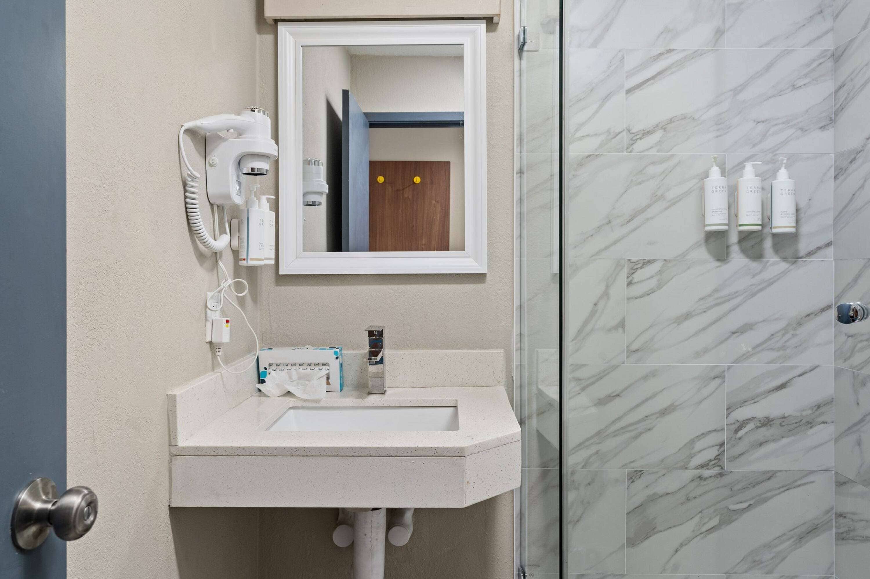 A bathroom with a white sink, a hairdryer, and toiletries on the wall.