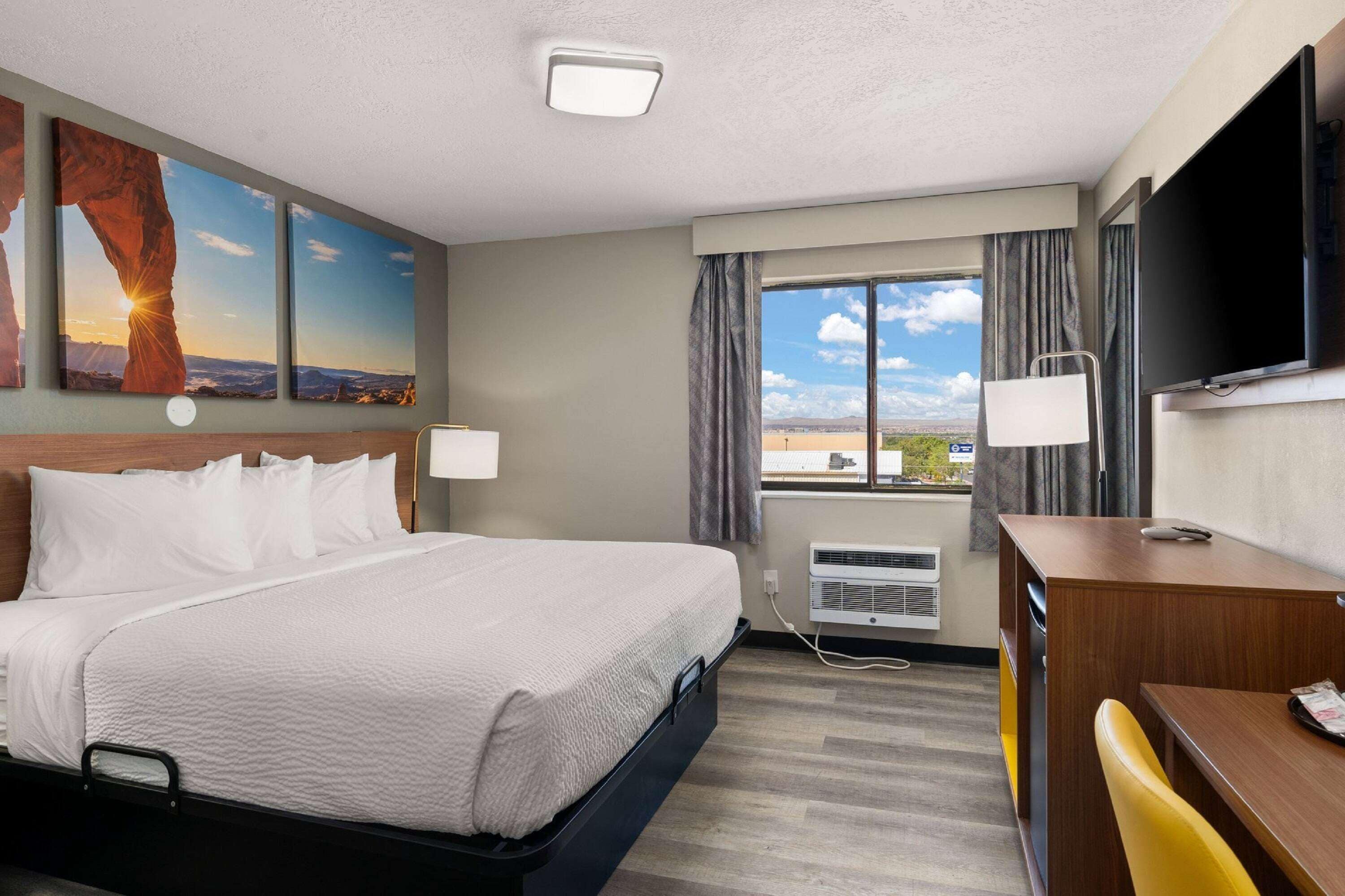 A hotel room with a bed, a desk, a TV, and a window with a view of the desert.