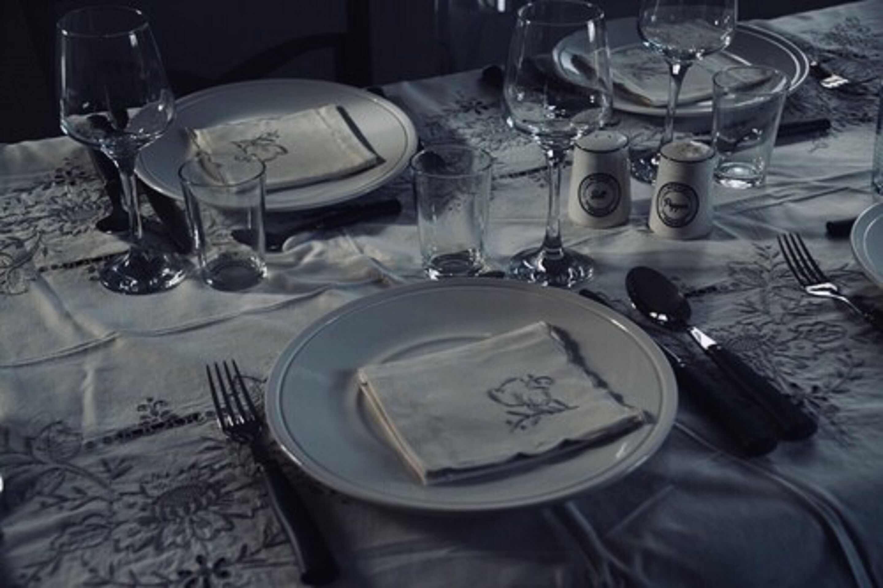 Una mesa dispuesta para una comida, con platos, cubiertos, vasos y salero.