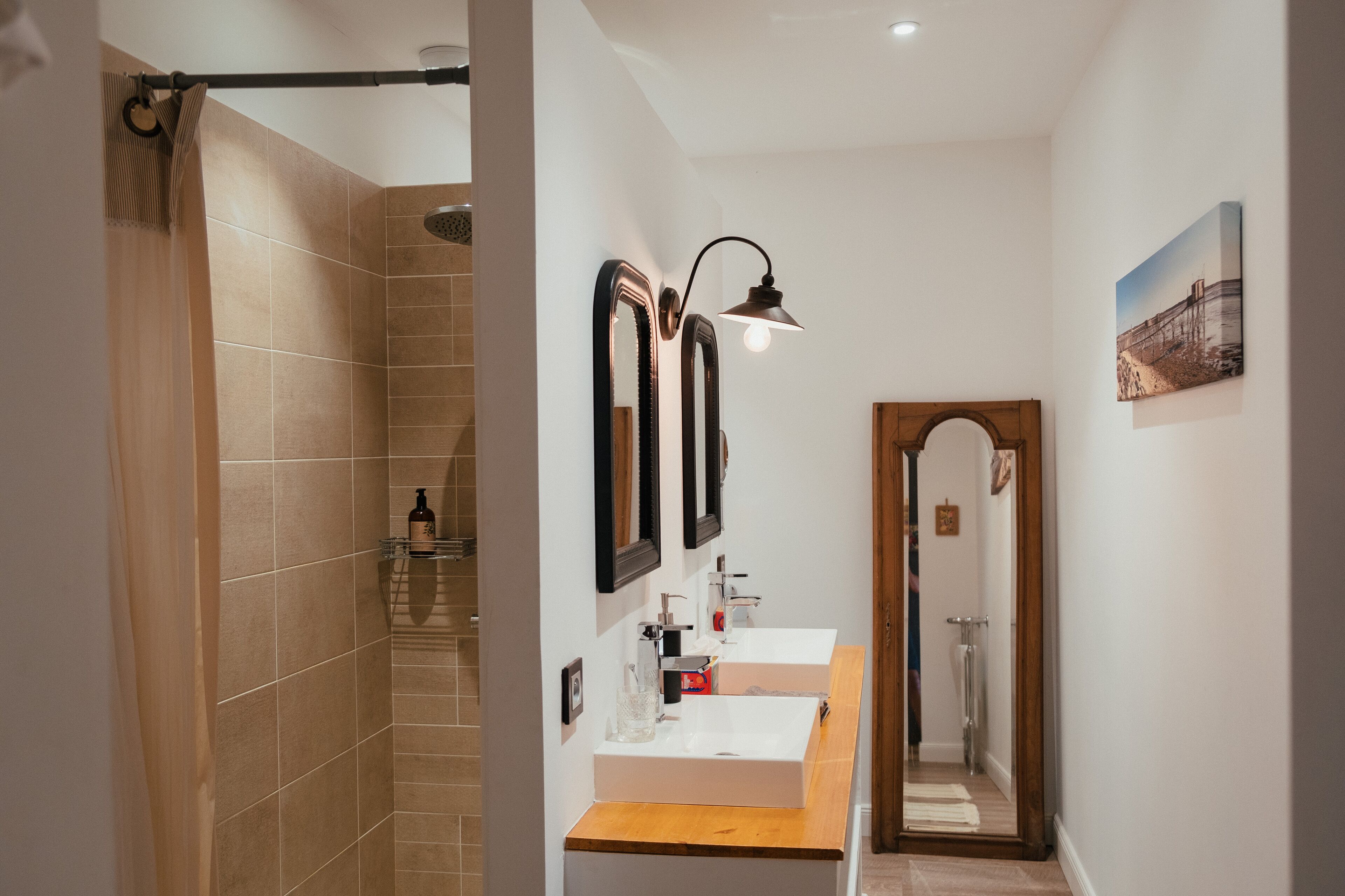 A modern bathroom with two sinks, a shower, and a mirror with a light fixture.