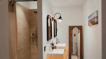 A modern bathroom with two sinks, a shower, and a mirror with a light fixture.