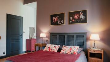 Une chambre à coucher comprenant un lit, deux lampes fixées au mur, une commode et deux tableaux représentant des motifs floraux.