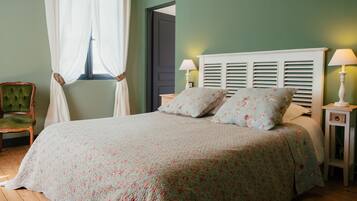 A bedroom with a bed, two bedside lamps, a green chair, and a window with white curtains.