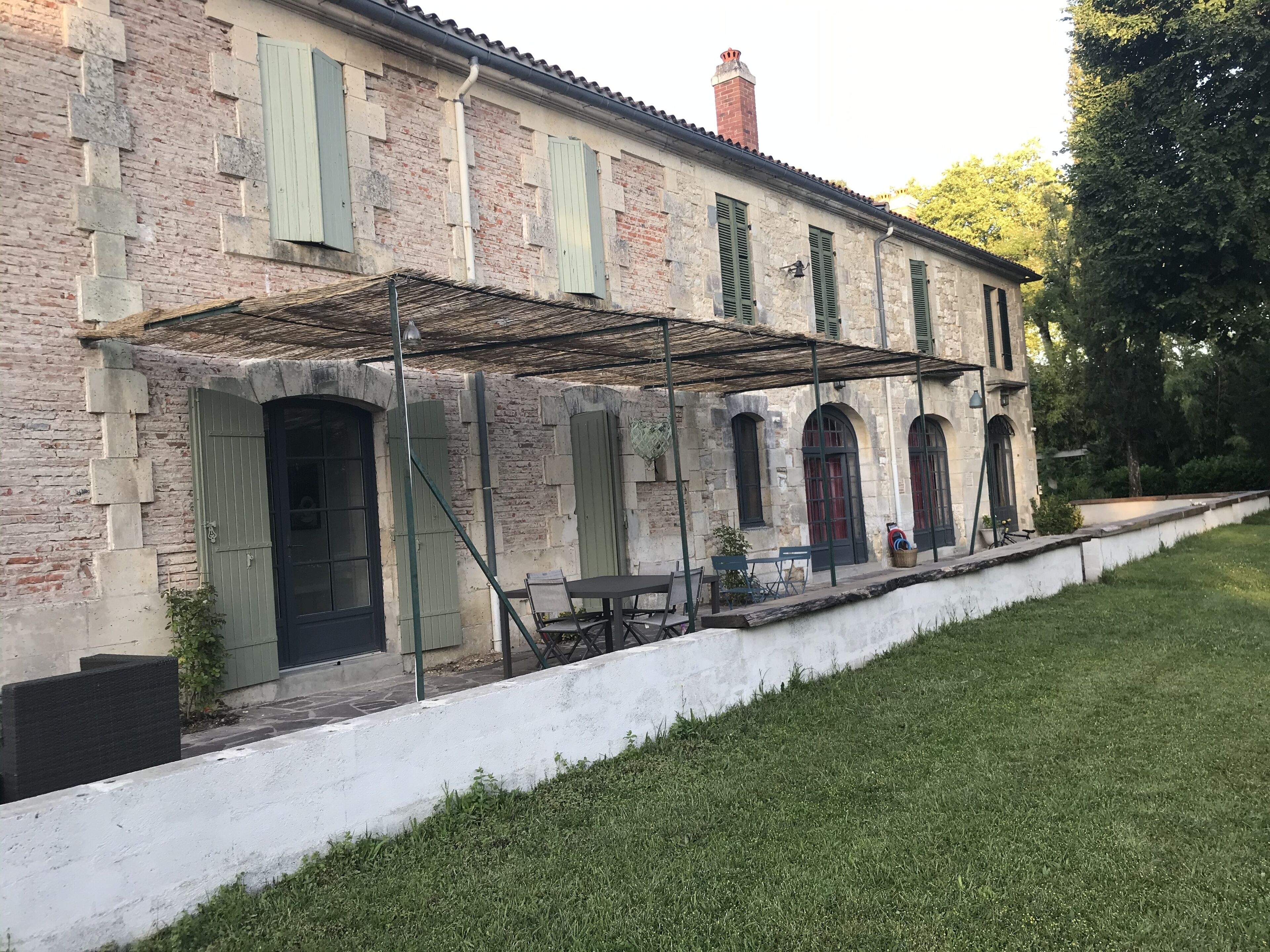 Ein Steinhaus mit grünen Fensterläden, einer überdachten Terrasse und einer weißen Fassade.