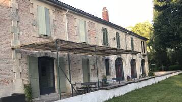 Ein Steinhaus mit grünen Fensterläden, einer überdachten Terrasse und einer weißen Fassade.