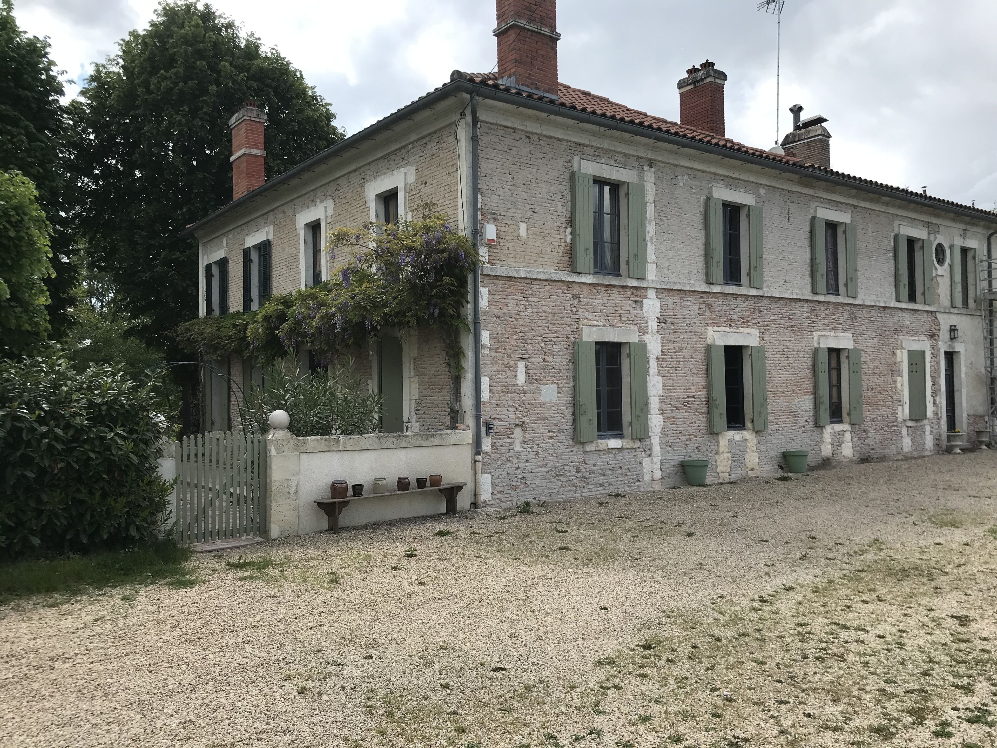 A two-story stone building with green shutters, a gravel driveway, and a white picket fence.