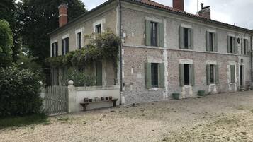 A two-story stone building with green shutters, a gravel driveway, and a white picket fence.