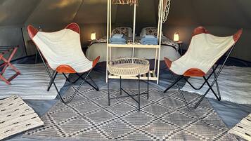 A tented accommodation with a bed, two chairs, a table, and a hanging light fixture.