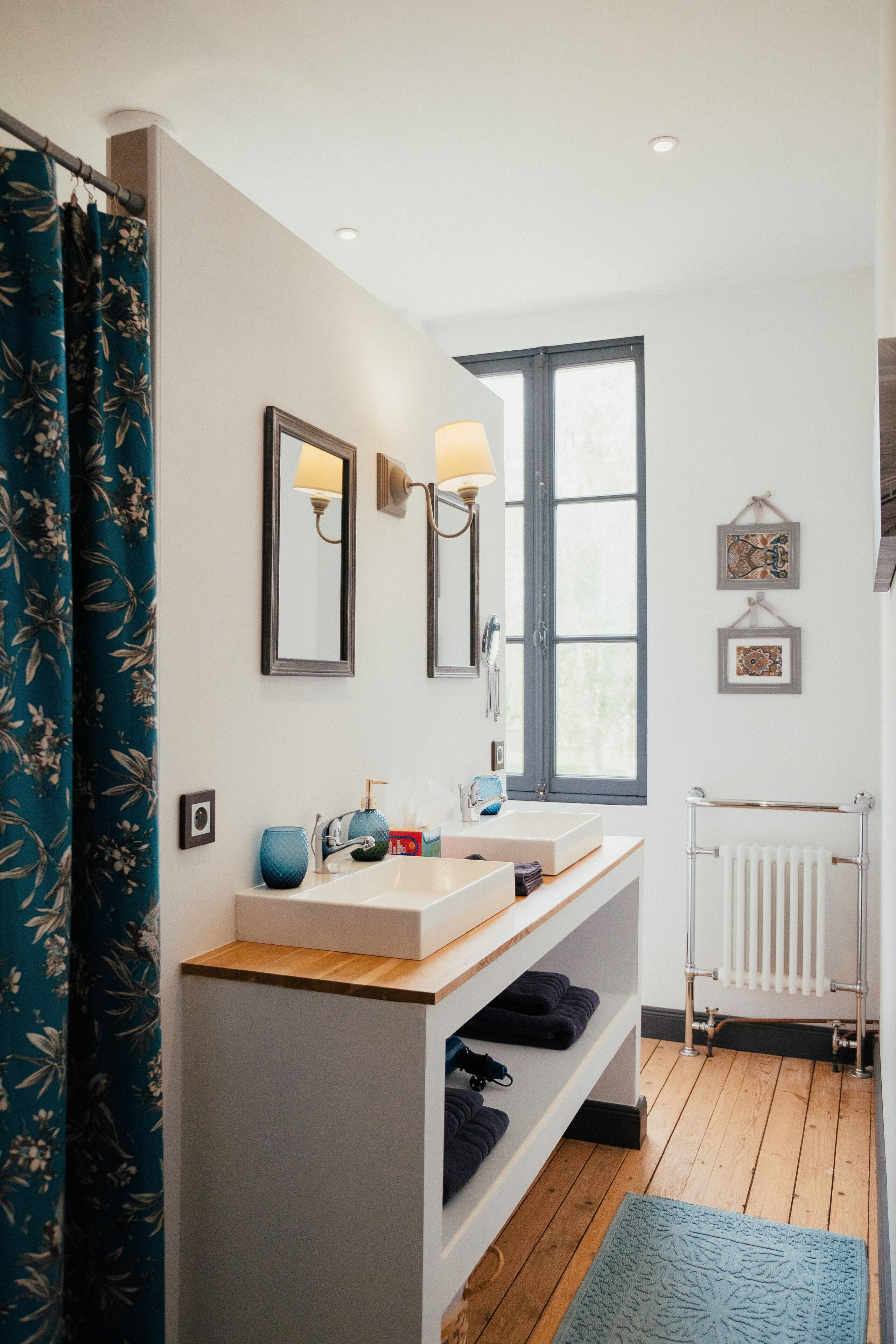 Een badkamer met een houten wastafelmeubel, twee wasbakken, een spiegel, een raam en een handdoekrek.