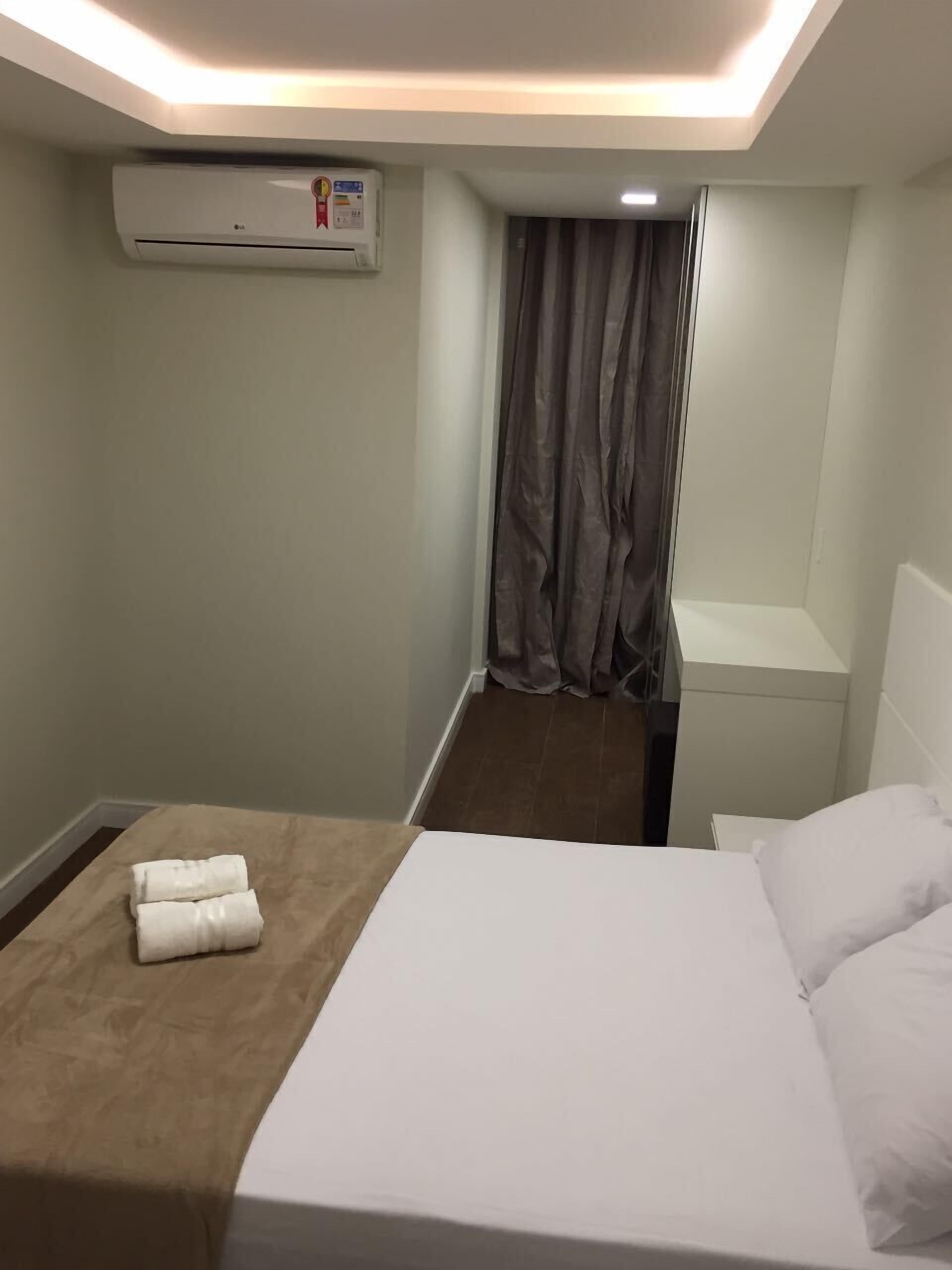 Una camera d'albergo con un letto, un comodino, un condizionatore d'aria a muro e una tenda.