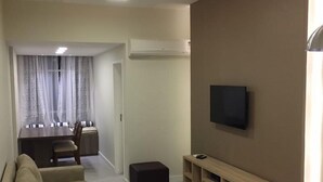 Ein modernes Wohnzimmer mit einer Couch, einem Fernseher und einem Essbereich mit Tisch und Stühlen.