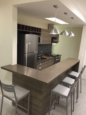 Une cuisine moderne dotée d’un îlot central, d’appareils électroménagers en acier inoxydable et de luminaires suspendus.