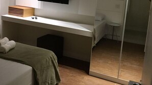 Ein modernes Hotelzimmer mit Bett, Schreibtisch, Flachbildfernseher, kleinem Tisch und Schiebetürenschrank.