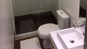 Ein kleines Badezimmer mit einer Duschkabine, einer weißen Toilette und einem weißen Waschbecken.