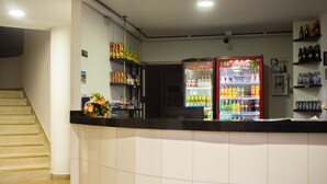 Zona de recepción de un hotel con un refrigerador de Coca-Cola, estantes con aperitivos y una escalera.