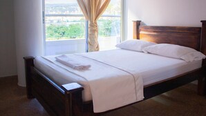Una cama bien hecha con cabecera de madera, una ventana con cortinas y vistas al exterior.