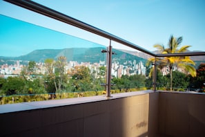 A balcony with a glass barrier, offering a view of a cityscape with buildings and palm trees. - Hotel Plaza Mayor Itagui (Itagüí)