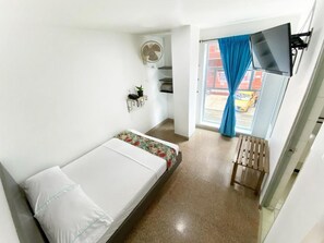 A compact room with a bed, a small table, a fan, and a window with curtains. - Hotel Plaza Mayor Itagui (Itagüí)