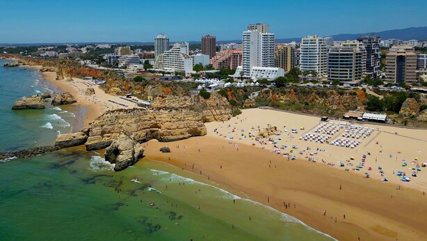 A coastal cityscape with a sandy beach, rocky cliffs, and high-rise buildings. - T2 standing Praia da Rocha (21052 / AL) (Portimão)