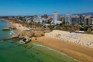 A coastal cityscape with a sandy beach, rocky cliffs, and high-rise buildings. - T2 standing Praia da Rocha (21052 / AL) (Portimão)