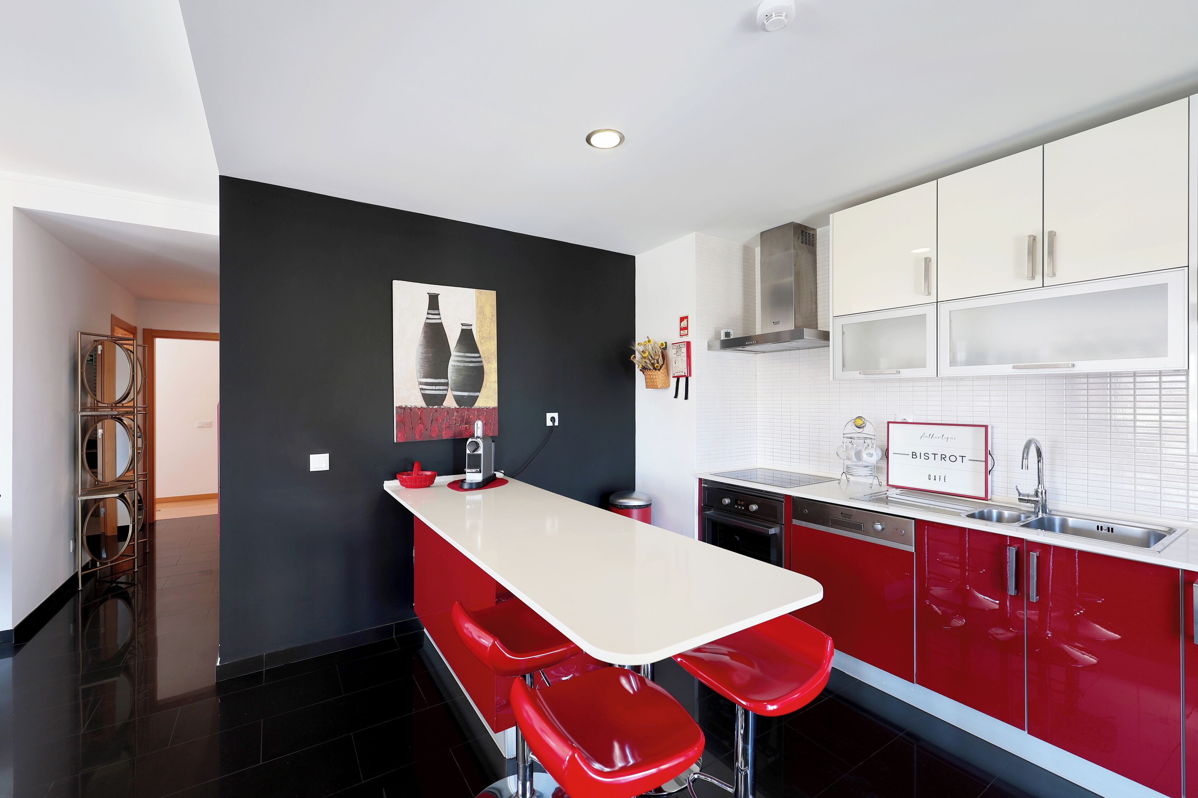 A modern kitchen with a black accent wall, red bar stools, and a white countertop.