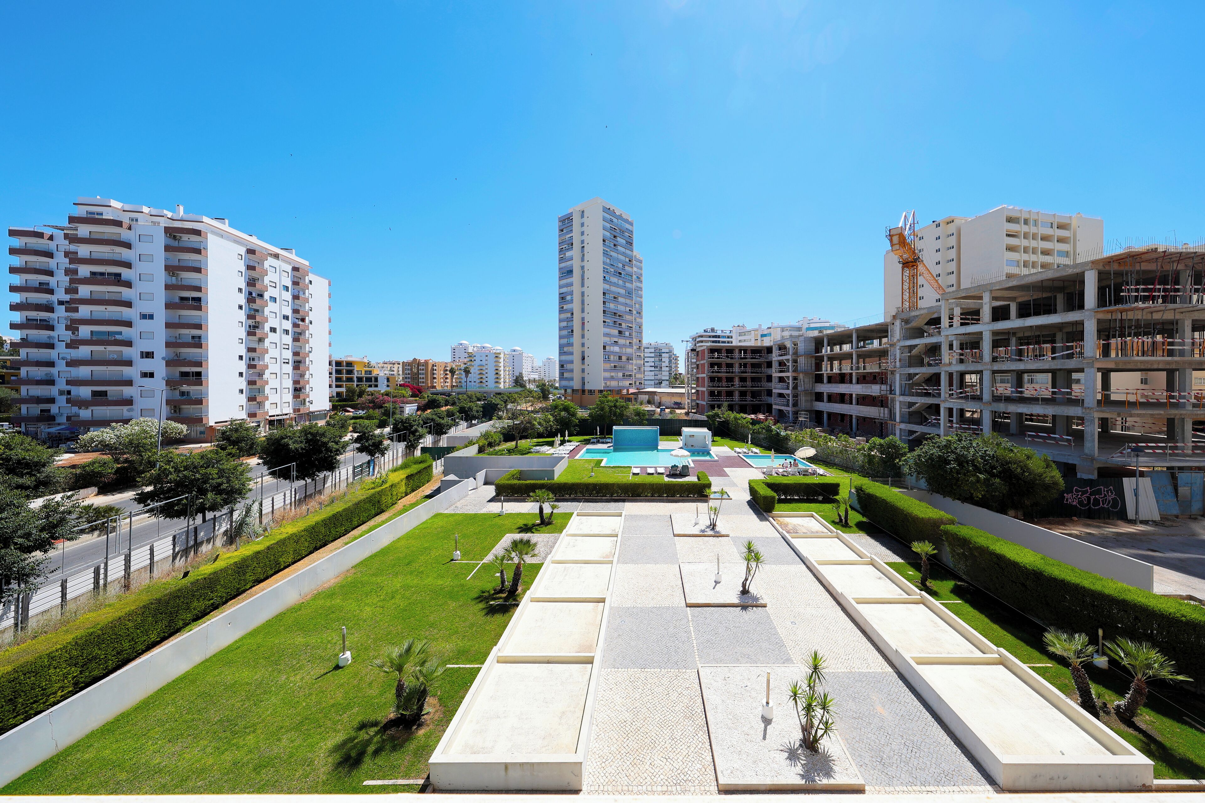 Un área urbana moderna con edificios altos, una plaza central con piscina y abundante vegetación.